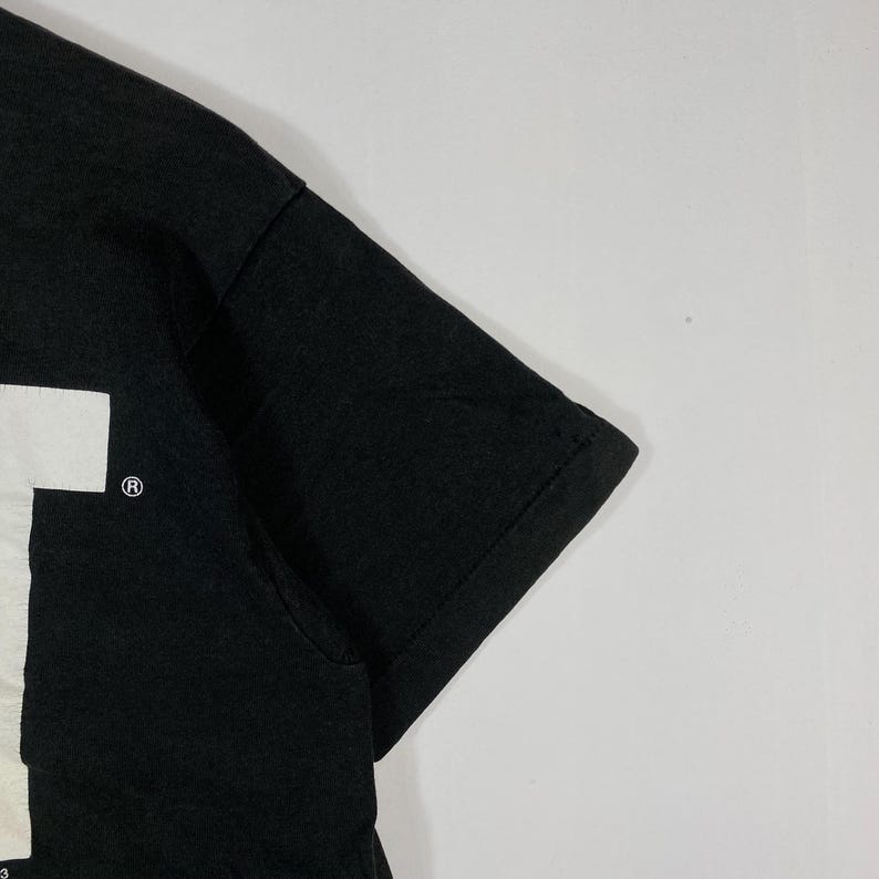 May include: Black short-sleeved t-shirt with a white graphic on the front. The shirt has a crew neck and a classic fit. The sleeve is visible in the image.