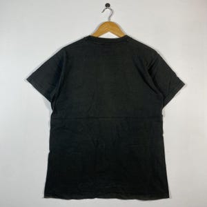 May include: A black t-shirt hanging on a wooden hanger. The short-sleeved shirt is made of a soft material and has a slightly faded appearance. The shirt is displayed against a plain white background.