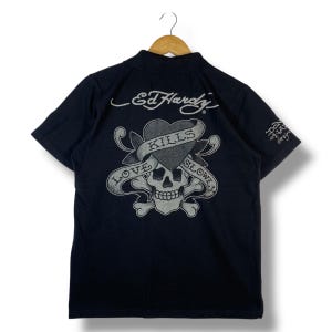 May include: Black polo shirt with a graphic design on the back. The design features a skull, heart, and the words "LOVE KILLS SLOWLY" in a banner. The Ed Hardy logo is visible above the graphic.