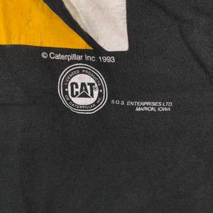 May include: Black fabric with a yellow and white design. The image features the Caterpillar Inc. 1993 logo, a CAT logo within a circle, and text indicating S.O.S. Enterprises Ltd., Marion, Iowa.