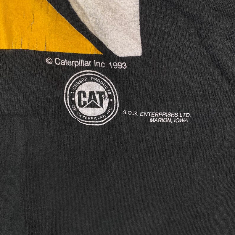 May include: Black fabric with a yellow and white design. The image features the Caterpillar Inc. 1993 logo, a CAT logo within a circle, and text indicating S.O.S. Enterprises Ltd., Marion, Iowa.