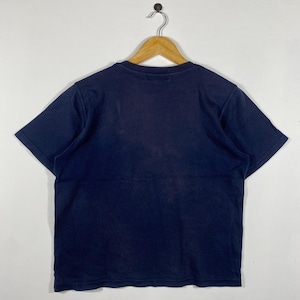 May include: A navy blue short-sleeved t-shirt hanging on a wooden hanger. The shirt is made of a soft material and has a simple design. The shirt is displayed against a white background.