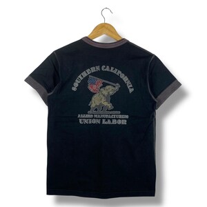 May include: Black t-shirt with a grey collar and sleeves. The back of the shirt features an illustration of an elephant holding an American flag, with the text "SOUTHERN CALIFORNIA" above and "ALLIED MANUFACTURING UNION LABOR" below.
