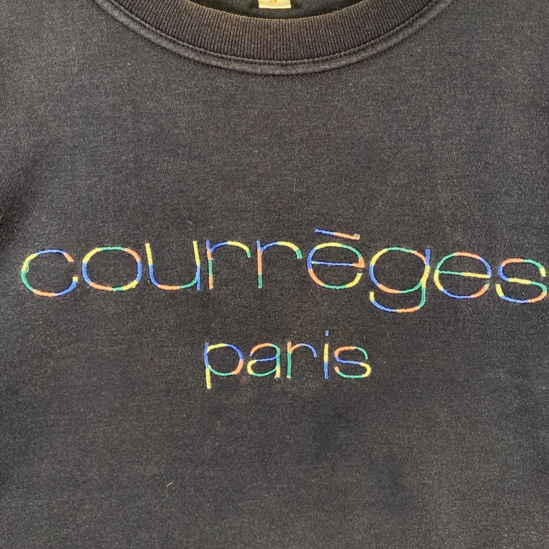 May include: A navy blue sweatshirt with the embroidered text "courr&egrave;ges paris" in a rainbow color scheme. The text is centered on the chest of the sweatshirt. The sweatshirt has a crew neck.
