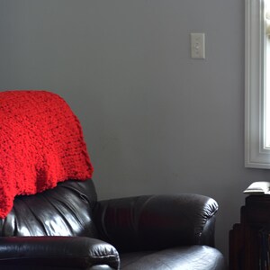 May include: A red knitted blanket on a black leather recliner. The room has grey walls and a window with a lamp. The lamp has a stained glass shade. A small table is next to the chair with a laptop.