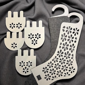 Puede incluir: Un calcetín gris con tarjetas de exhibición de calcetines blancas y una forma de calcetín blanca. Las tarjetas de exhibición tienen un diseño floral y los números 40-41, 42-43, 44-45, 46-47 y 48-49. La forma del calcetín tiene un diseño floral.