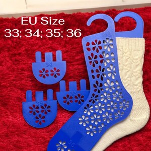 Op de afbeelding: Een blauwe sokvorm met bloemenpatroon en een crèmekleurige sok op een rode ondergrond. De vorm heeft een hanger en is ontworpen voor EU-maten 33, 34, 35 en 36. Er zijn ook blauwe maatmarkeringen.