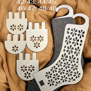 Puede incluir: Un par de calcetines grises con una horma blanca y varios moldeadores de calcetines blancos. La horma tiene un estampado floral. El texto "EU Size 42/43; 44/45; 46/47; 48/49" es visible.