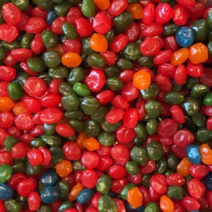 Puede incluir: Primer plano de un montón de coloridas gominolas. Las gominolas son de varios colores, incluyendo rojo, verde, naranja y azul. Los caramelos tienen una textura brillante y suave y están apilados, llenando el encuadre.