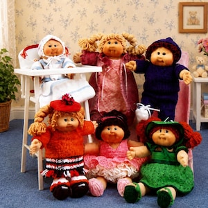 May include: A collection of Cabbage Patch Kids dolls. The dolls are dressed in various knitted outfits, including dresses, sweaters, and hats. One doll is seated in a high chair. The dolls have yarn hair and rosy cheeks.