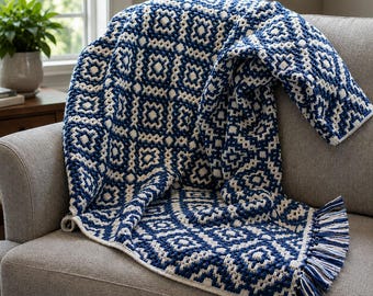 May include: A navy blue and cream-colored geometric patterned throw blanket with fringe detail. The blanket is draped over a gray sofa. The pattern features a repeating diamond and square design. The fringe is a mix of navy and cream-colored yarn.