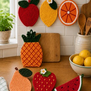 May include: A collection of colorful, crocheted fruit-shaped kitchen items, including an apple, lemon, orange slice, pineapple, pear, strawberry, and watermelon slice. The items are displayed on a wooden countertop and hanging on hooks.