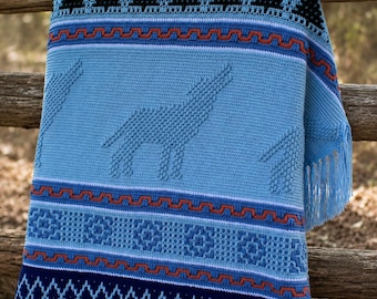 May include: A light blue crochet blanket featuring a repeating pattern of howling wolves in a textured stitch. The design includes horizontal bands of black triangles, orange geometric lines, and a dark blue border with a white cross-stitch pattern.