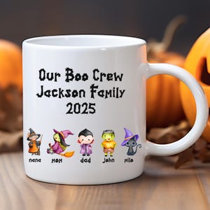 May include: White ceramic mug with the text "Our Boo Crew Jackson Family 2025". The mug features cartoon illustrations of Halloween characters, including a witch, vampire, and Frankenstein's monster. The names "nana", "mom", "dad", "John", and "Milo" are printed below the characters.