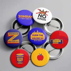 May include: A collection of colorful campaign buttons. The buttons feature text such as "Zohran for New York City", "No Kings", and "Turn the Volume Up! Mayor Mamdani". The buttons are round with pin backs and various graphic designs.