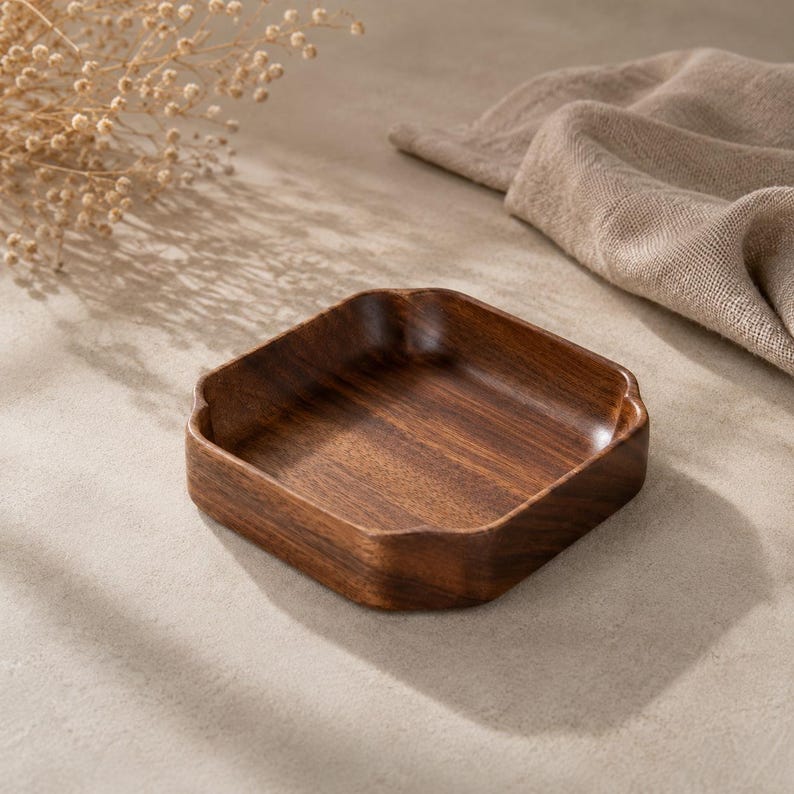 May include: A square wooden tray with rounded corners and a deep, dark brown wood grain finish. The tray features a smooth, polished surface with slightly raised edges, showcasing the natural texture and rich color variations of the wood.