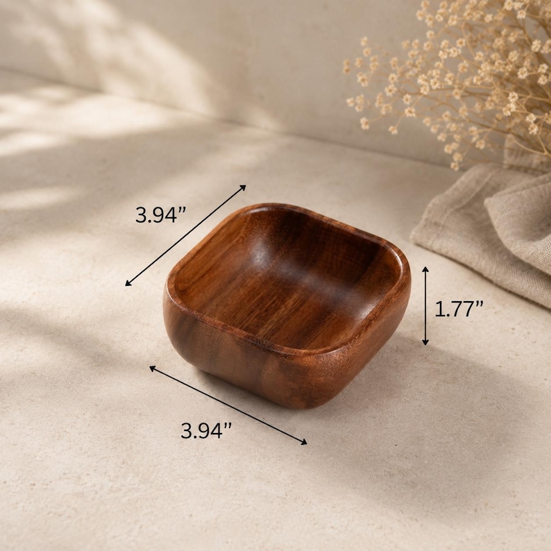 May include: A square wooden bowl with rounded corners and a smooth, dark brown grain finish. The bowl features dimensions of 3.94 inches in length, 3.94 inches in width, and 1.77 inches in height as indicated by the visible measurement labels.