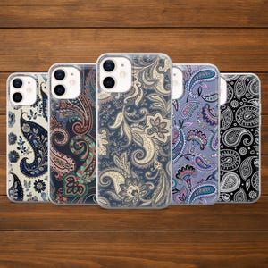 May include: Five phone cases featuring paisley patterns in navy, cream, burgundy, purple, and black. The cases are displayed on a wooden surface, highlighting the detailed floral designs. Each case is designed for a smartphone.