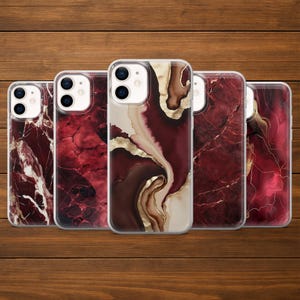 May include: Five phone cases with abstract designs. The cases feature a variety of patterns in shades of red, burgundy, cream, and gold. The designs resemble marble or flowing ink. The cases are displayed on a wooden surface.