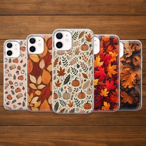 May include: Five phone cases with autumn-themed designs. The cases feature patterns of pumpkins, leaves, and foliage in shades of orange, brown, and beige. The cases are displayed on a wooden surface.