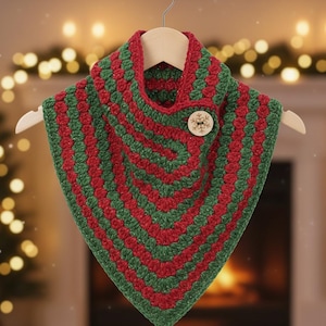 May include: A handmade, crocheted cowl in red and green stripes, with a wooden snowflake button closure. The cowl is displayed on a wooden hanger, perfect for holiday or winter wear.