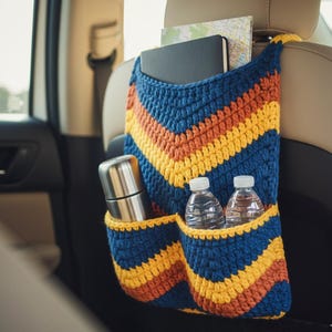May include: A blue, orange, and yellow crocheted car organizer hanging on a car seat. The organizer has pockets holding a stainless steel thermos, two water bottles, a notebook, and a map. The chevron pattern adds a decorative touch.