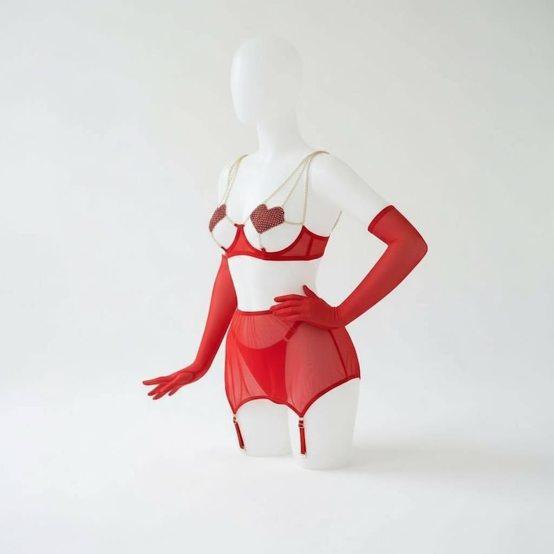 May include: Red lingerie set with heart-shaped accents on the bra cups and gold chain straps. The set includes a matching garter belt, underwear, and long gloves. The lingerie is displayed on a white mannequin against a white background.