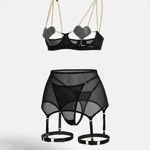 May include: Black lingerie set featuring a bra with heart-shaped rhinestone cups and gold chain straps. The set includes a matching garter belt with adjustable straps and a thong. The lingerie is made of sheer mesh fabric.