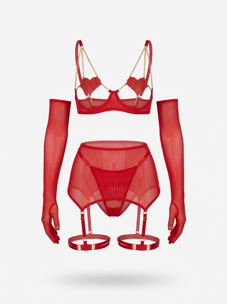 May include: A red lingerie set featuring a bra with heart-shaped embellishments and gold chain straps, a garter belt, a thong, and sheer gloves. The set is made of a sheer, lightweight fabric. The bra has underwire support.