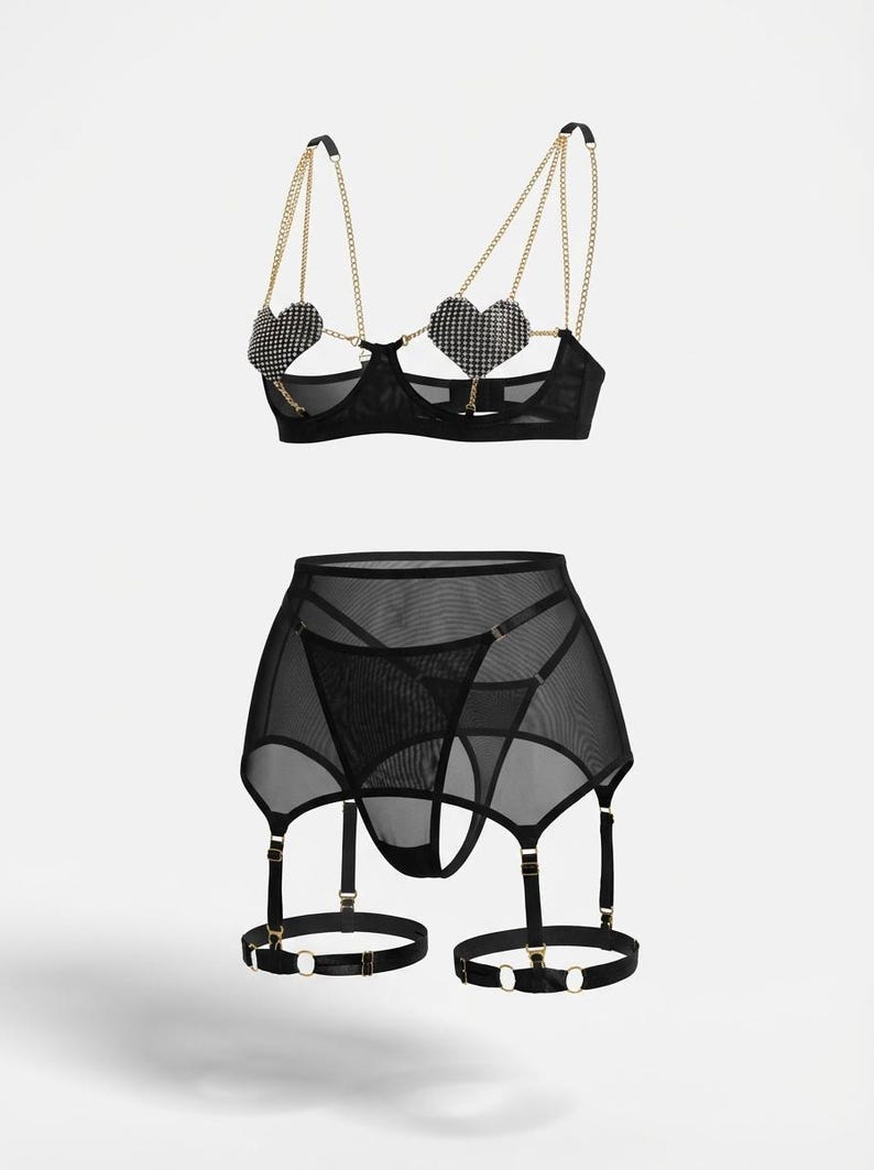 May include: Black lingerie set featuring a bra with heart-shaped rhinestone cups and gold chain straps, paired with a matching garter skirt and thong. The set is made of sheer mesh fabric.