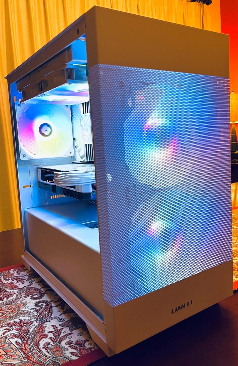 May include: A white computer case with a perforated front panel. The case has internal components illuminated by colorful LED lights. The brand name "LIAN LI" is visible on the lower right corner. The case is designed for high-performance computing.