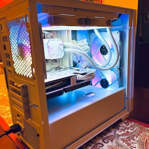 May include: A white computer case with internal components illuminated by blue and purple LED lights. The case features a graphics card labeled "GEFORCE RTX" and a CPU cooler. The text "THERMALRIGHT" is visible on the top of the case.