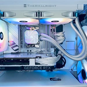 May include: A white computer case with internal components, including a graphics card labeled "GEFORCE RTX" and a CPU cooler. The case features multiple fans with colorful LED lighting. The brand "THERMALRIGHT" is visible at the top.
