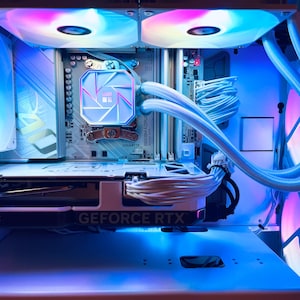 May include: Inside view of a computer case with components illuminated by blue, pink, and white LED lights. The graphics card reads "GEFORCE RTX". The cooling system has a white tube and a light-up logo. The case fans are also lit up with colorful lights.