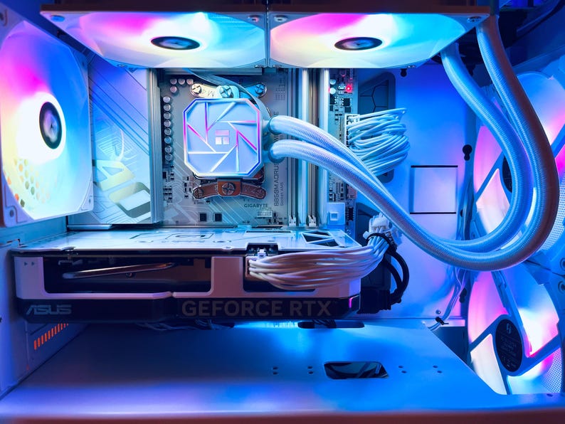 May include: Inside view of a computer case with components illuminated by blue, pink, and white LED lights. The graphics card reads "GEFORCE RTX". The cooling system has a white tube and a light-up logo. The case fans are also lit up with colorful lights.