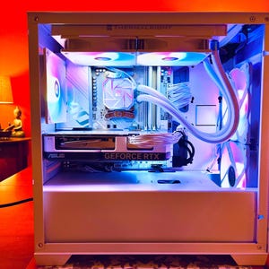 May include: A white computer case with internal components illuminated by blue and purple LED lights. The case features a graphics card with "GEFORCE RTX" printed on it. The components are neatly arranged, showcasing a modern PC build.