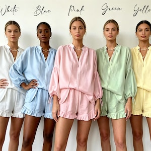 May include: Five women modeling matching pajama sets in white, blue, pink, green, and yellow. Each set includes a long-sleeved top with a drawstring neckline and shorts with a ruffled hem. The word "White", "Blue", "Pink", "Green", and "Yellow" are written above each woman.
