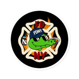 以下が含まれることがあります： サングラスとFDNYの帽子をかぶった漫画のアリゲーターが描かれた丸いステッカー。アリゲーターは、赤色のFDとNYの文字が入った消防署のマルタ十字の前にいます。アリゲーターは注射器と医療器具を持っています。