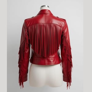 Könnte beinhalten: Rote Lederjacke mit Fransen am Rücken und an den Ärmeln. Die Jacke hat ein klassisches Design mit Kragen, Knöpfen und taillierter Taille. Die Fransen verleihen dem Kleidungsstück eine einzigartige, stilvolle Note.