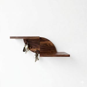 Può includere: Un portachiavi moderno in legno scuro con un design geometrico unico. Il portachiavi presenta due ripiani e una sezione semicircolare con ganci per chiavi. Due mazzi di chiavi sono appesi ai ganci. Il portachiavi è montato su una parete bianca.