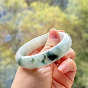 May include: A smooth, polished bangle bracelet crafted from translucent white stone featuring distinct, irregular patches of deep forest green color throughout the circular band, showcasing a glossy finish and a rounded, substantial profile.