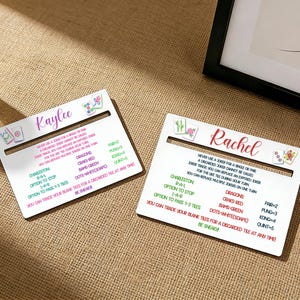 May include: Two white Mahjong score cards, each with a name in cursive script, "Kaylee" and "Rachel". The cards display game rules and scoring information in black and red text, with floral and tile illustrations. They rest on a textured, neutral-toned surface, suitable for Mahjong players.