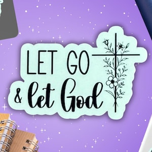 May include: A collection of stickers, notebooks, a water bottle, and a smartphone are arranged on a purple surface. The stickers and notebooks feature the text "LET GO & let God" with a cross and floral design. The water bottle is blue.
