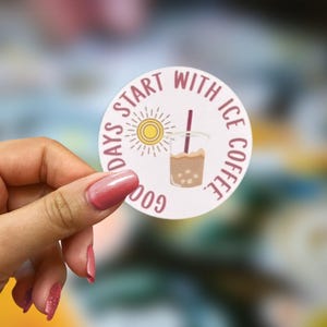 May include: A circular sticker with the phrase "Good days start with ice coffee." The design includes a sun and an iced coffee illustration. The sticker is white with maroon and brown details.