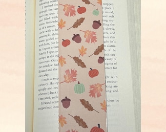 May include: A rectangular bookmark with a beige background, adorned with a repeating pattern of autumn leaves, pumpkins, and acorns in shades of orange, brown, and green. The bookmark is placed on an open book. The number "259" is visible at the bottom.