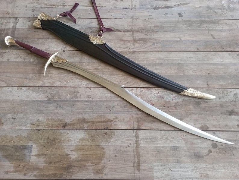 May include: A curved sword with a metallic blade, a maroon leather-wrapped handle, and gold-colored wing-shaped accents on the crossguard. It is accompanied by a black scabbard featuring matching gold-colored wing details and maroon leather straps.