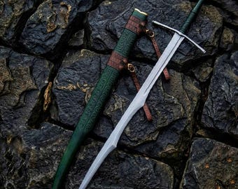 May include: A medieval sword with a silver blade and a green and brown leather-wrapped handle and scabbard. The sword is lying on a dark, textured stone surface. The scabbard has decorative patterns.