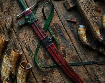 May include: A medieval-style sword with a red and brown leather-wrapped hilt and scabbard. The sword features a silver crossguard and a green leather strap. The background includes wooden elements, nails, and drinking horns.