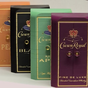 May include: Four rectangular boxes arranged in a row, each featuring the Crown Royal logo with a crown on a cushion. The boxes are colored orange, black, light green, and purple, with gold lettering and circular knobs on the front panels.
