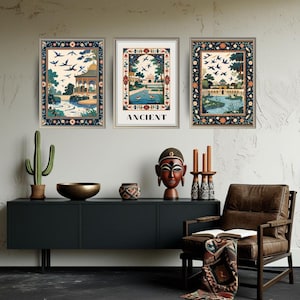 May include: Three framed art prints with intricate designs. The prints depict scenes with buildings, water features, and flying birds, framed with ornate borders. One print features the word "ANCIENT". The artwork is displayed above a dark cabinet with decorative items and a leather armchair.